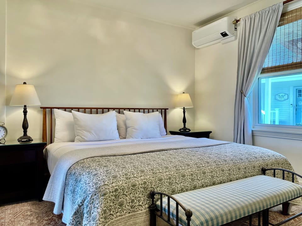 Room 10 features a plush king bed, crisp linens, bedside lighting, and a sunny window with garden views—perfect for a restful stay at Admiral's Quarters Inn in Boothbay Harbor.
