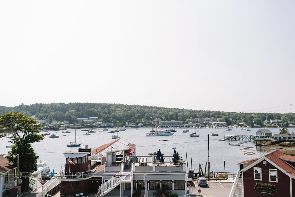 Take in sweeping views of Boothbay Harbor from Admiral's Quarters Inn—featuring sailboats, waterfront dining, and the iconic Tugboat Inn, all set against a peaceful coastal backdrop.