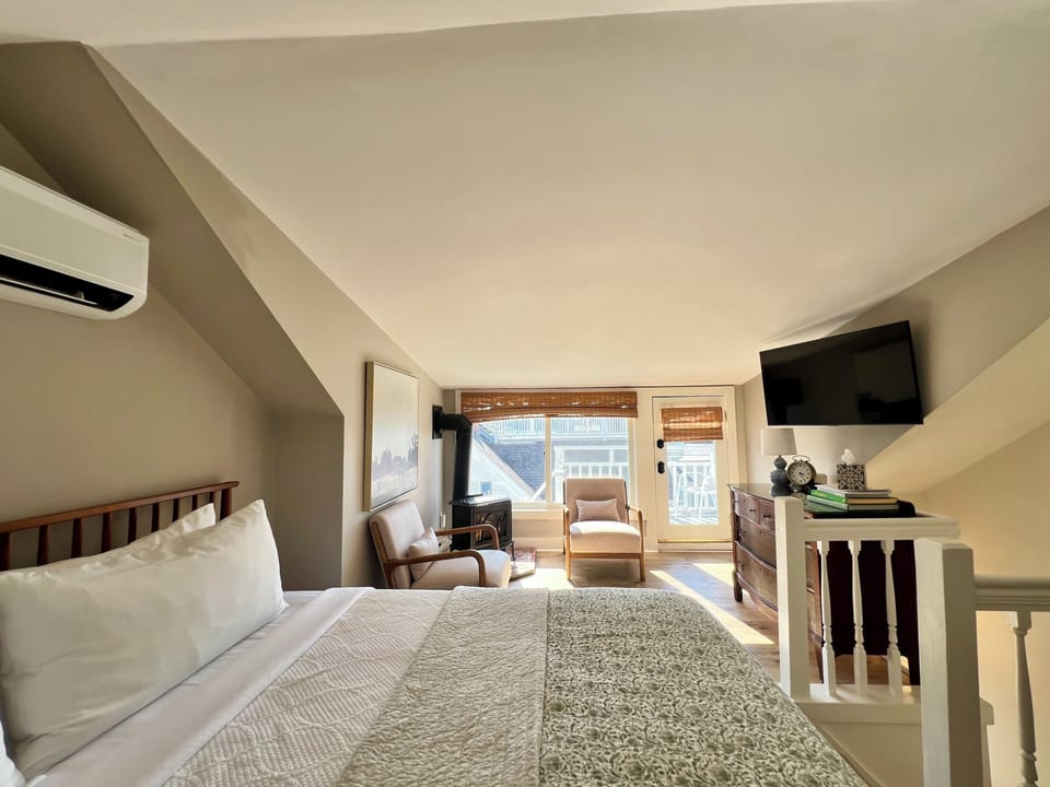 Unwind in Room 12's cozy upper-level king suite, featuring natural light, a sitting area, flat-screen TV, and charming sloped ceilings—just steps from the harbor and all that Boothbay has to offer.