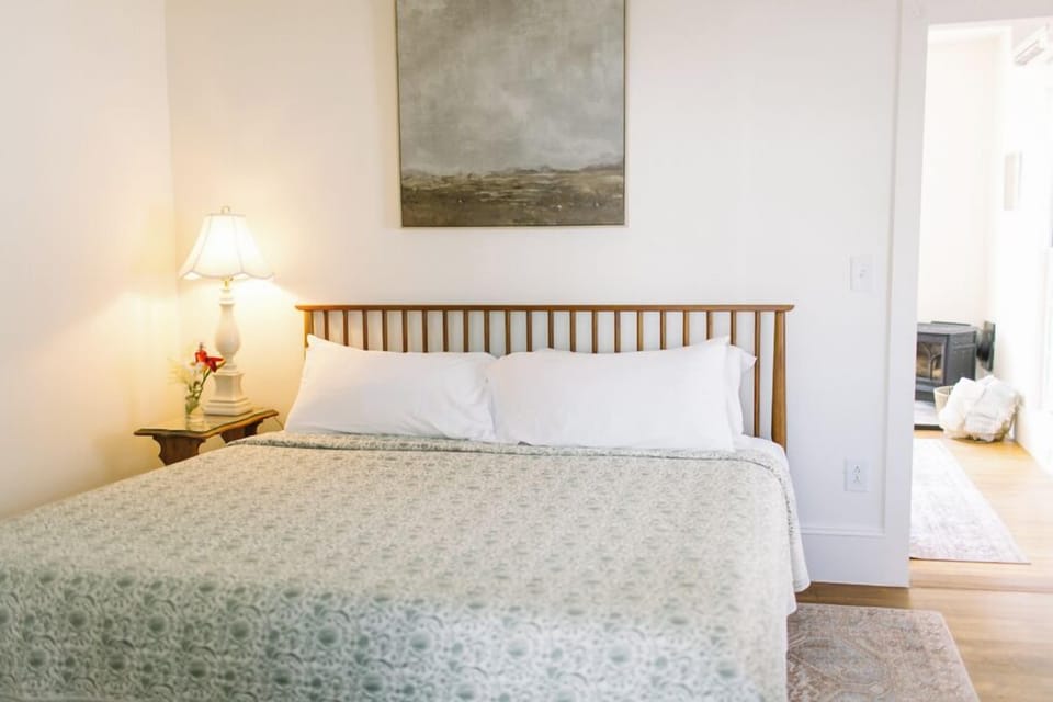 Relax in Room 13's peaceful king bedroom featuring a plush bed, soft lighting, and tranquil coastal decor—just steps from your private balcony and Boothbay Harbor's waterfront beauty.