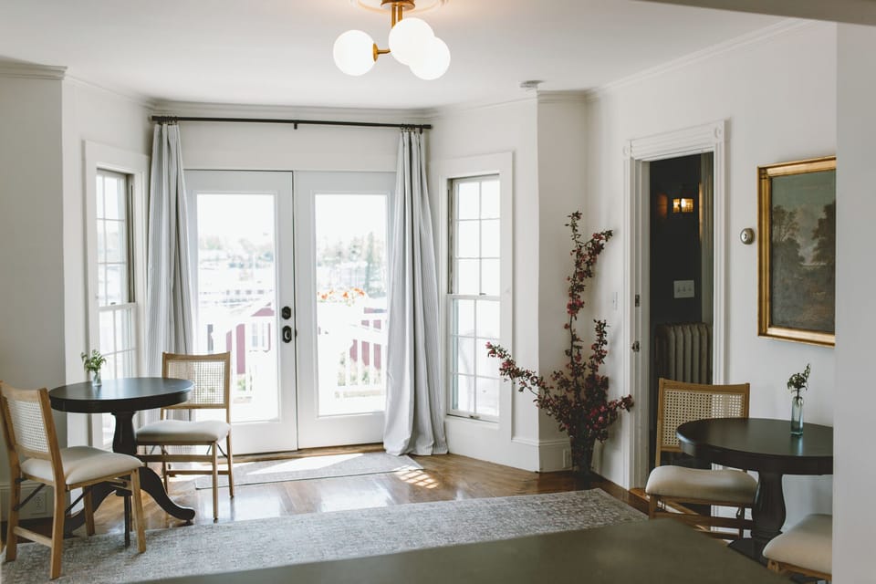 Enjoy peaceful moments in this sunlit common area at Admiral's Quarters Inn, featuring French doors, harbor views, and cozy café seating—perfect for coffee, reading, or planning your Boothbay Harbor adventures.