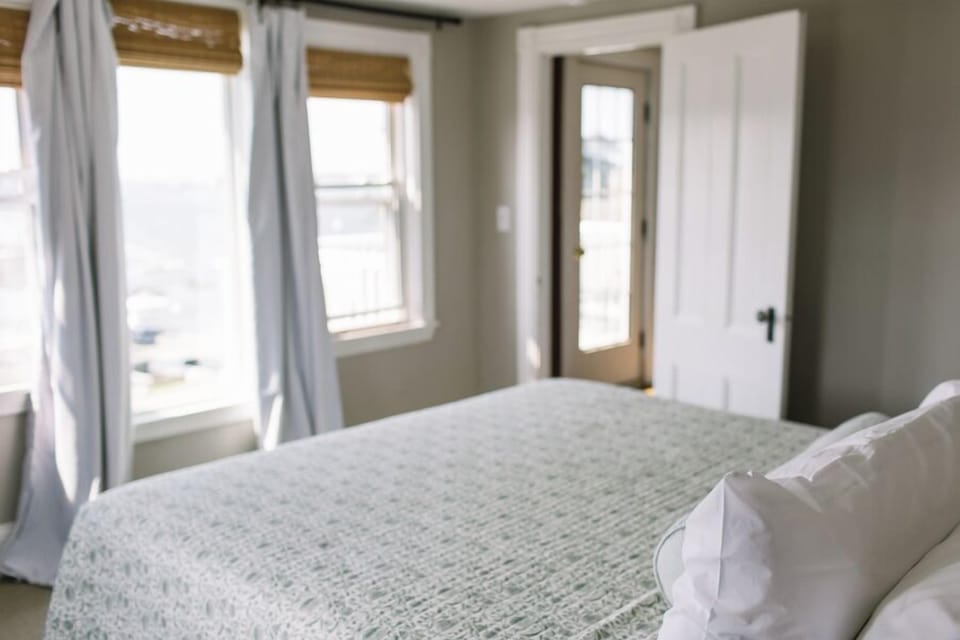 Room 15 features soft natural light, serene harbor views, and a cozy bed with crisp linens—plus direct access to a private balcony for the perfect Boothbay Harbor escape.