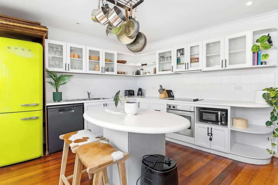 Our fully equipped, bright kitchen is a chef's dream! It features a vibrant retro fridge, ample white cabinets, a central island with seating, a sink, dishwasher, stove, oven, microwave, and a stylish toaster. Everything you need for delicious meals!