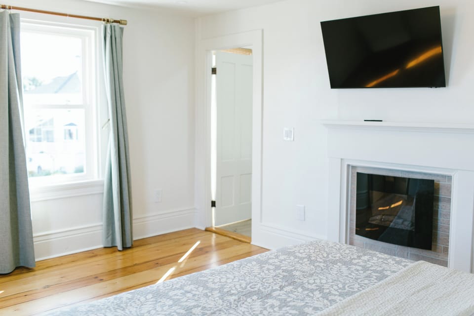 Room 4 at Greenleaf Inn features a queen bed, large windows with garden views, hardwood floors, a smart TV, and a cozy fireplace—perfect for a relaxing Boothbay Harbor escape.