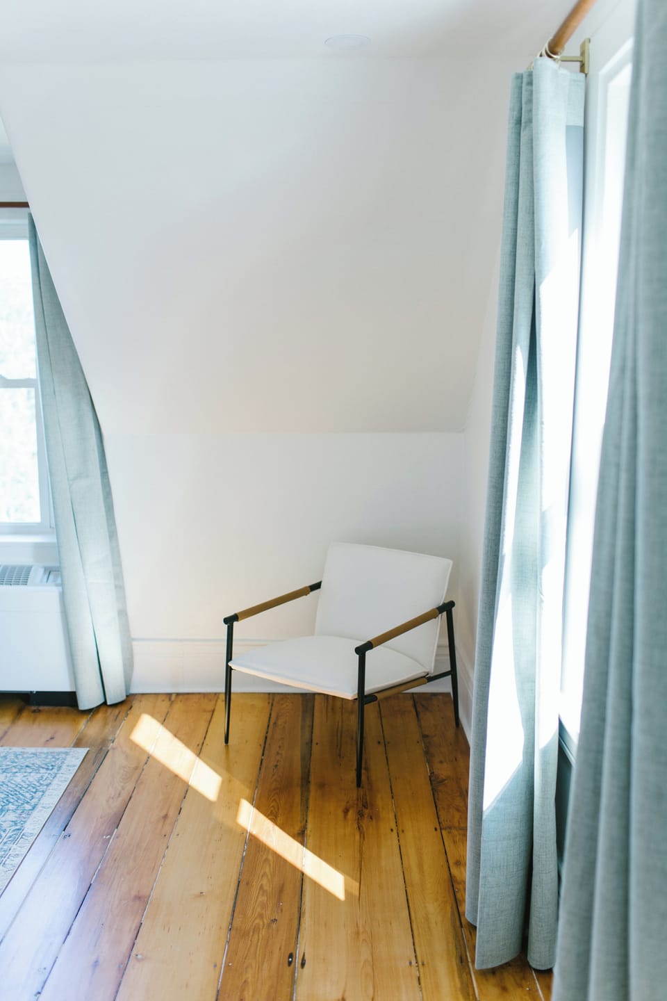 Unwind in this peaceful corner of Room 4, featuring a modern accent chair, hardwood floors, and soft natural light—perfect for reading or relaxing in Boothbay Harbor, Maine.