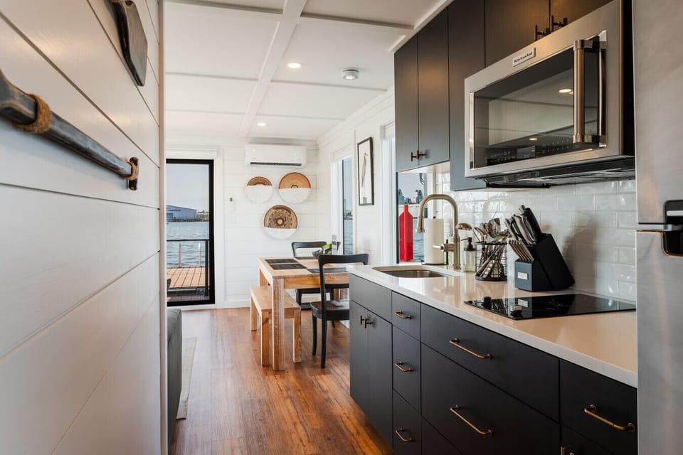 Modern galley kitchen with matte black cabinets, KitchenAid microwave, gold hardware, and a four-seat dining table by the window overlooking the marina.