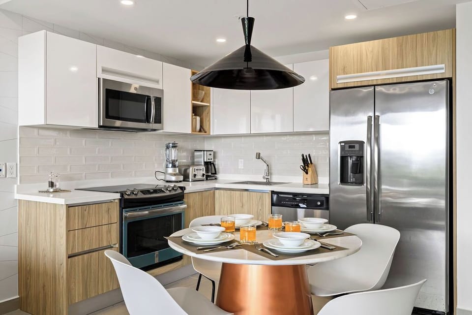 Step into your well-equipped kitchen where crisp white counters meet warm wood tones. Gather around the sleek table for breakfast with fresh juice and coffee, ready to fuel your adventures.