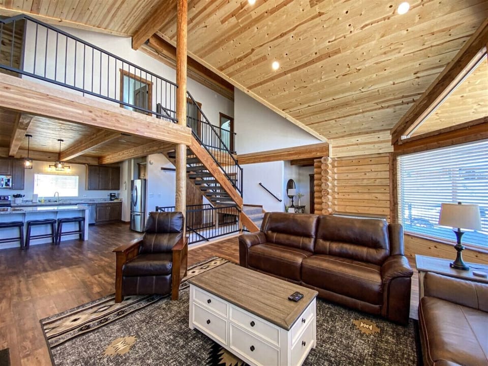 Spacious cabin great room with cozy leather seating, vaulted ceilings, and an open kitchen layout.