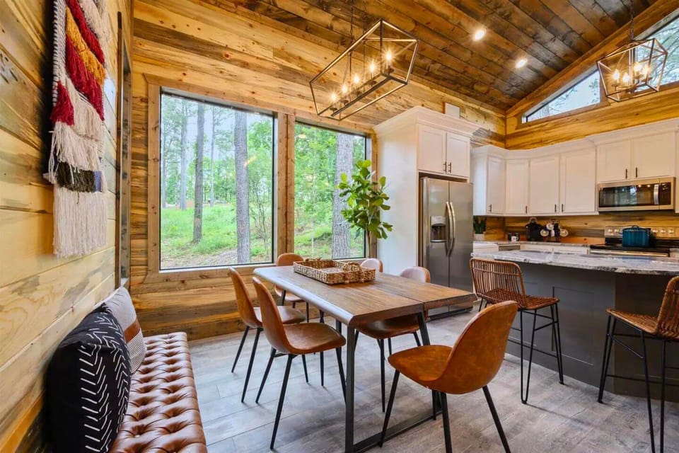 Enjoy meals in this dining area featuring a modern wooden table with leather chairs and a view of the greenery through large windows.