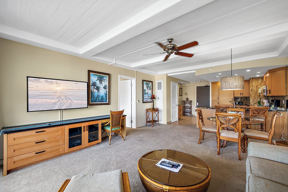 Relax in your open-concept living space with vaulted ceilings, tropical decor, and a ceiling fan. The dining area flows into a fully equipped kitchen, all bathed in natural light—perfect for your island getaway.