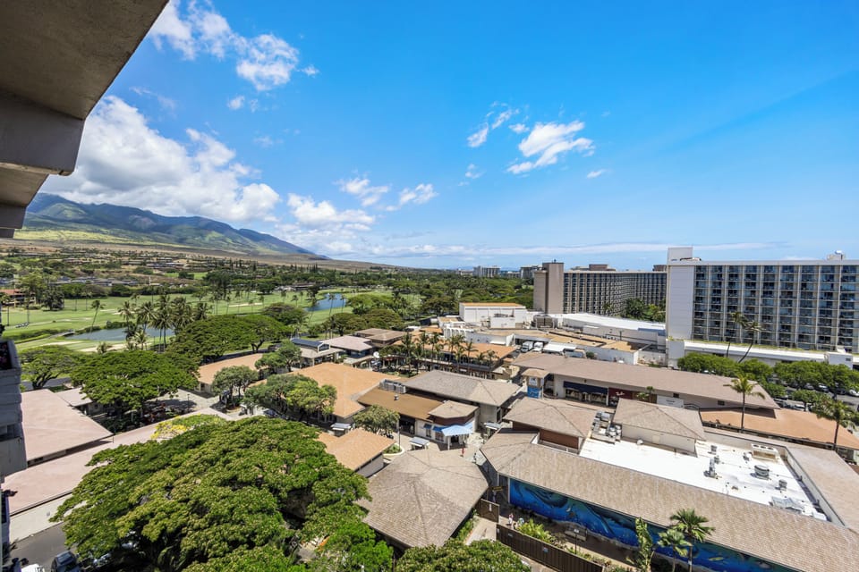 Elevated daytime view of the property's surrounding neighborhood, with mountains, golf course, and nearby resort buildings framing the tropical landscape.