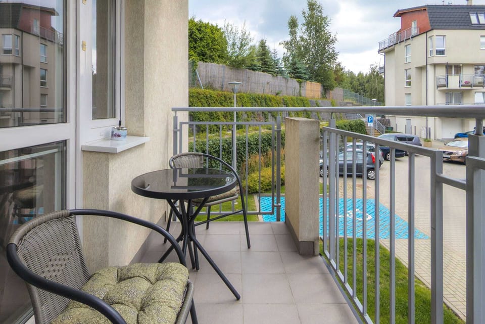 A balcony with a table and chairs, overlooking a quiet neighborhood with greenery.