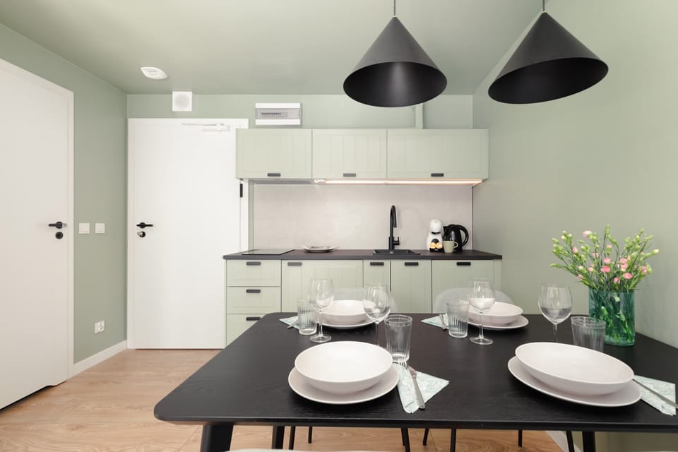 A bright dining space with a modern table, chairs, and large windows letting in natural light, complemented by neutral curtains.