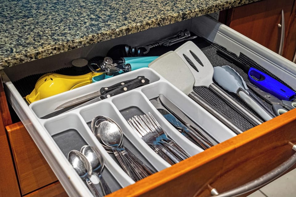 Organized kitchen drawer with essential utensils and tools under a granite countertop.
