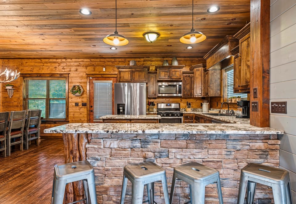 Welcoming kitchen bar with stone finish and metal stools, flanked by wooden cabinets and modern appliances.