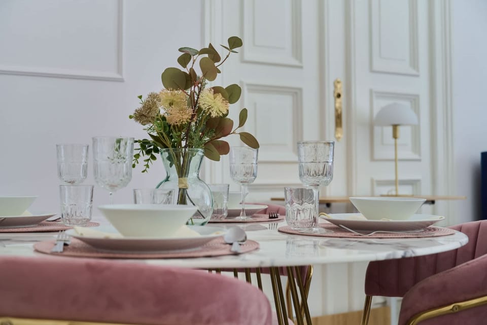A stylish dining space featuring a round glass table with pink velvet chairs and golden details for a touch of elegance.