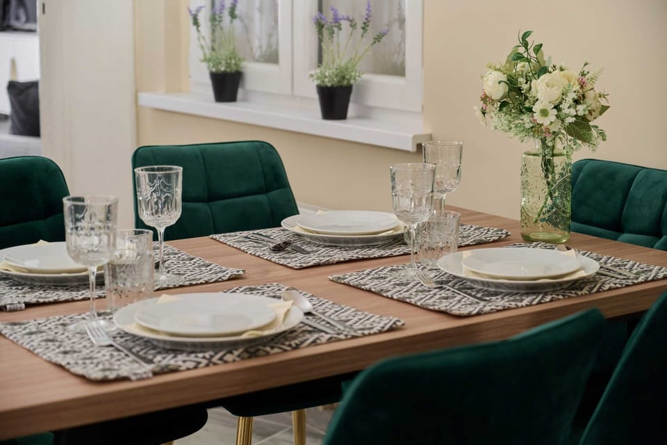 A small dining area with a chic wooden table, velvet green chairs, and modern interior lighting.