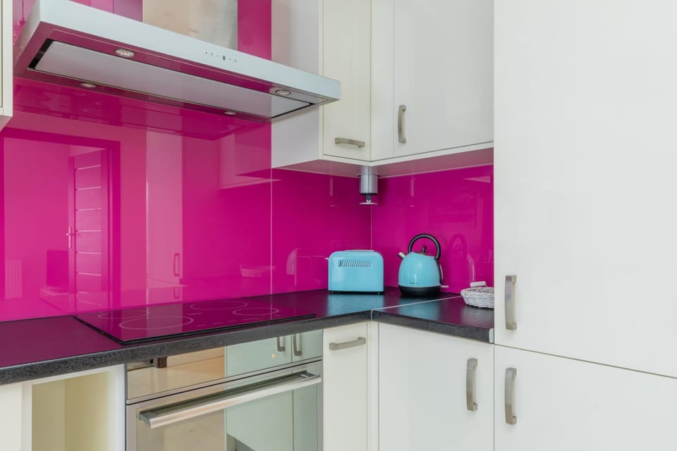 A contemporary kitchen with white cabinetry, high-gloss pink backsplash, and state-of-the-art appliances for a functional yet stylish look.