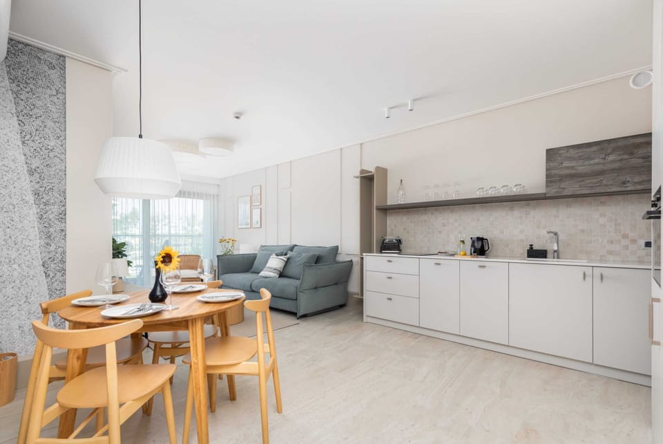 The dining area is designed with simplicity, featuring a wooden table and elegant chairs next to large windows.