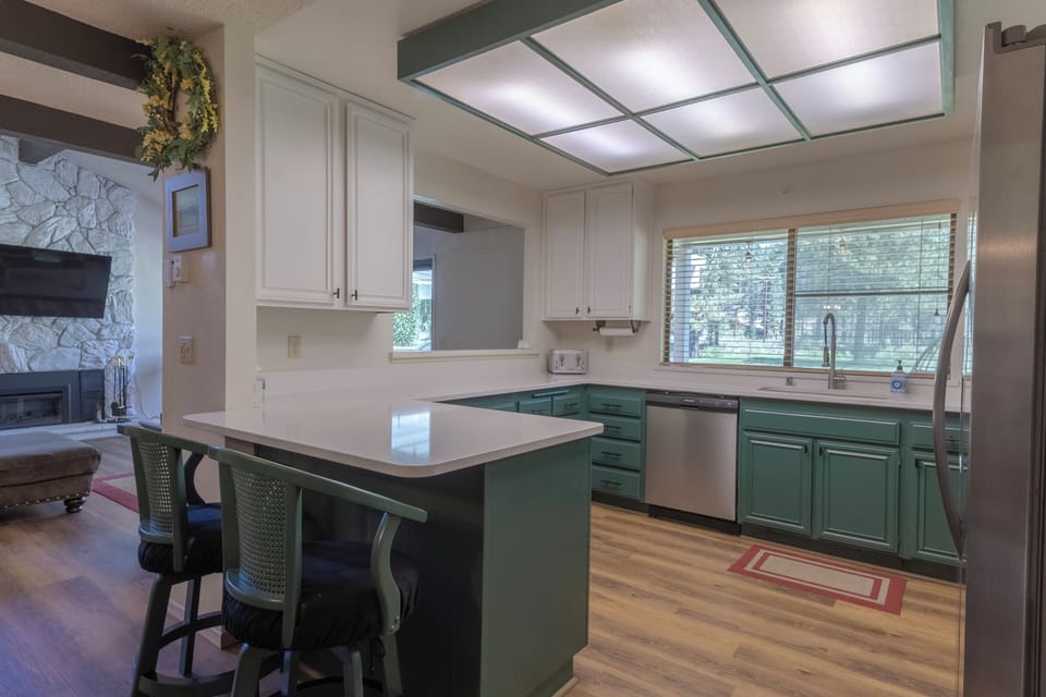 Bright open kitchen with bar seating, large windows, and forest views