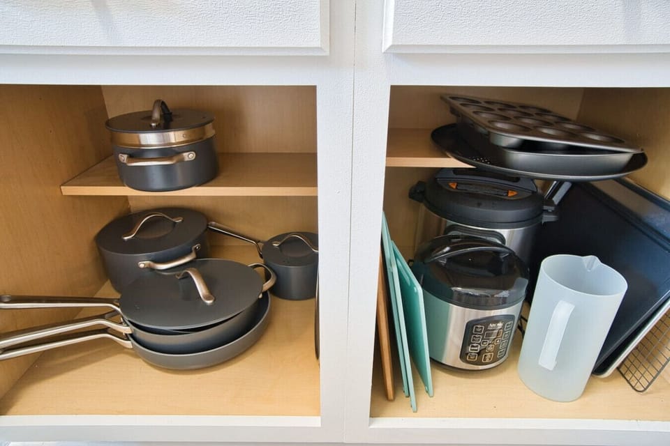 Cookware neatly organized: pots and pans with sleek lids on the left, cutting boards and an instant pot on the right, alongside baking trays and muffin pans for all your culinary creations.