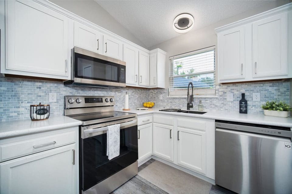 Stylish kitchen with stainless steel appliances, modern backsplash, and bright white cabinetry.