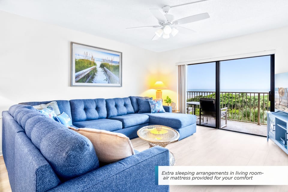 Bright and spacious living room with cozy seating and a TV, leading to a balcony.