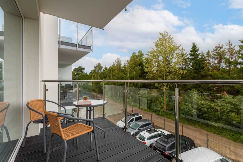 A balcony with a glass railing and outdoor furniture, offering views of the surrounding greenery.

