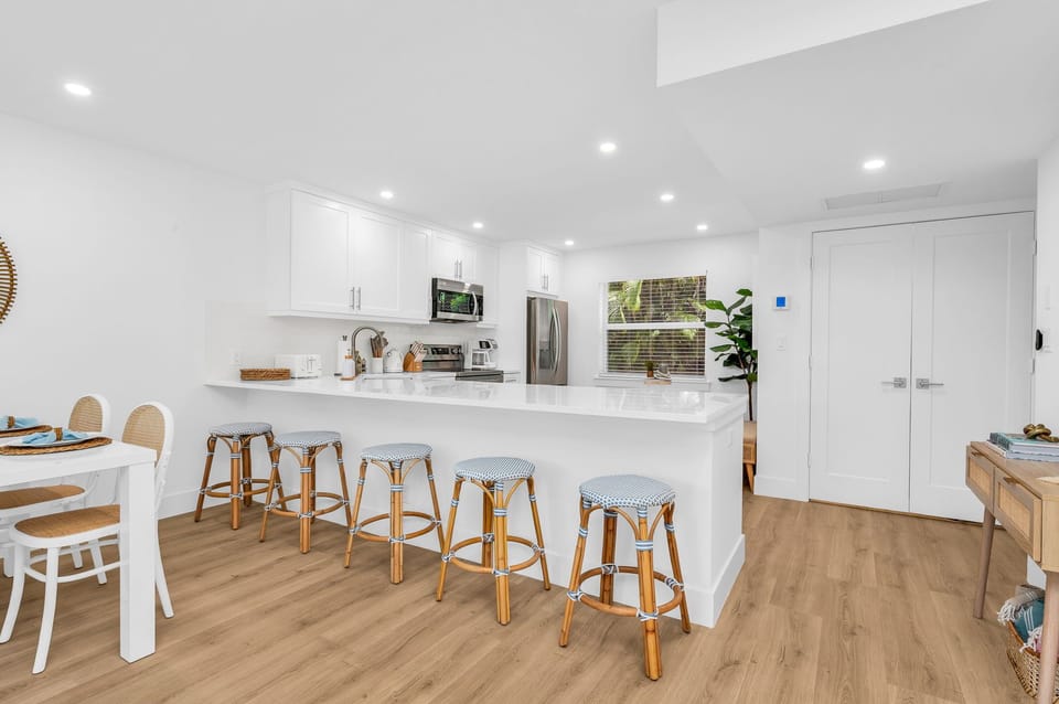 There are 5 sky-blue rattan bar stools at the impressively large quartz kitchen counter. The kitchen also has a kitchen nook with 2 upholstered rattan and cane benches, a modern contemporary white round table, and a decorative Fiddle tree.