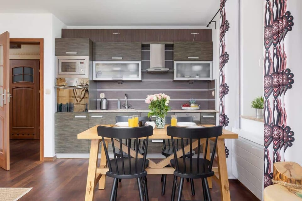 A wide-angle view of the open-plan kitchen and dining area, featuring wooden finishes and mountain-inspired curtains.







