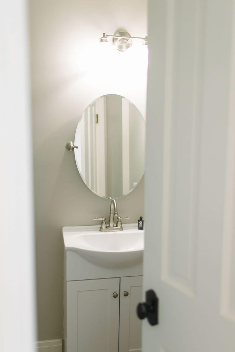 This clean, private ensuite bath features a sleek vanity, oval mirror, and soft lighting—offering guests a comfortable, stylish space to refresh during their Boothbay Harbor stay.