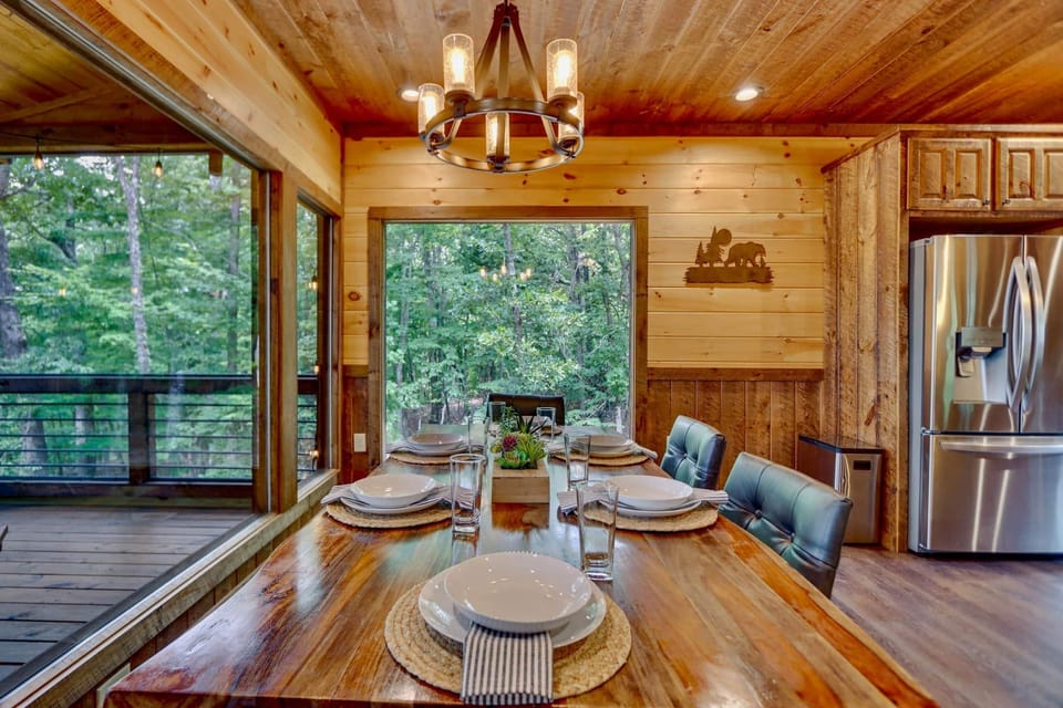 Rustic dining area with forest views, wood table, and chandelier in luxury North Georgia cabin