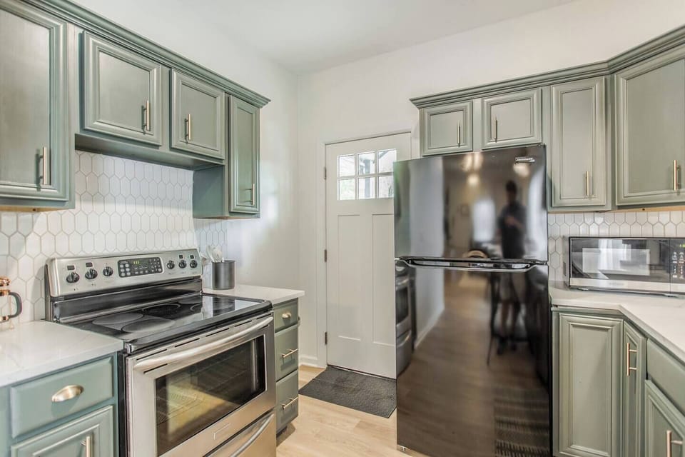Modern kitchen with stainless steel appliances, sleek hex-tile backsplash, and elegant sage green cabinetry