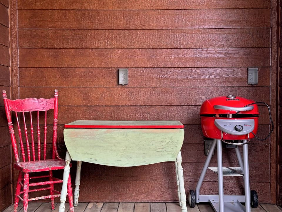 Red press-back chair, enamel-top dropleaf table & electric grill, on the porch.