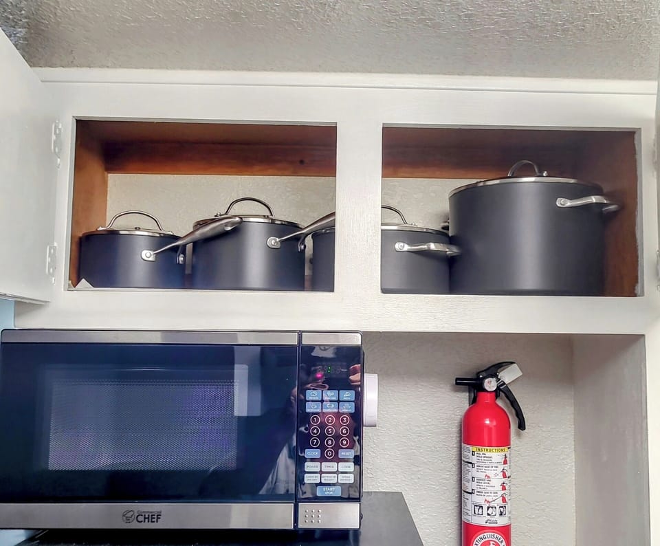 Cooking pots located over refrigerator. Microwave and fire extinguisher.