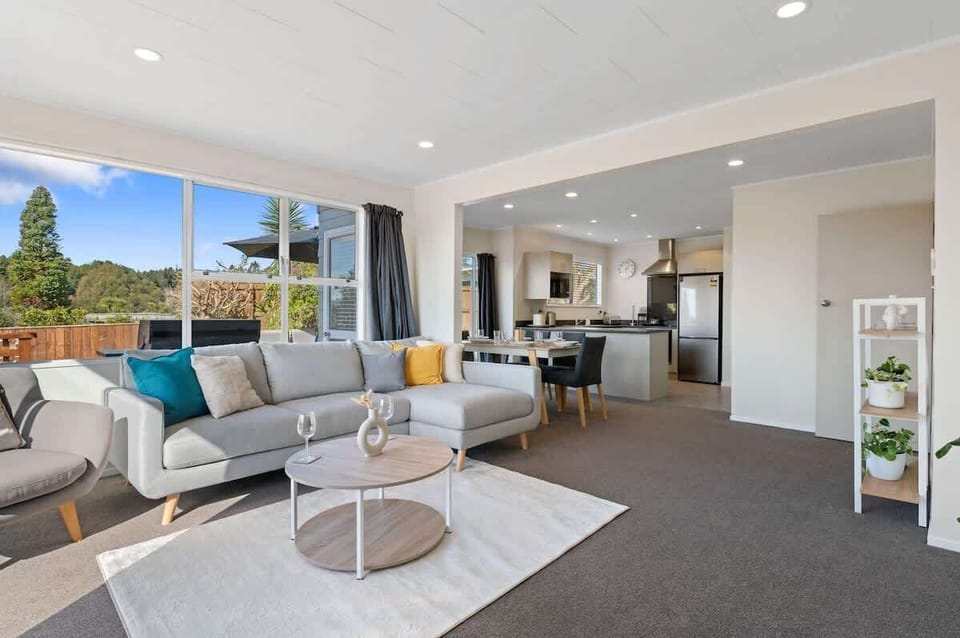 Bright open-plan living room with modern sofa, teal accents and large windows — Rotorua holiday home