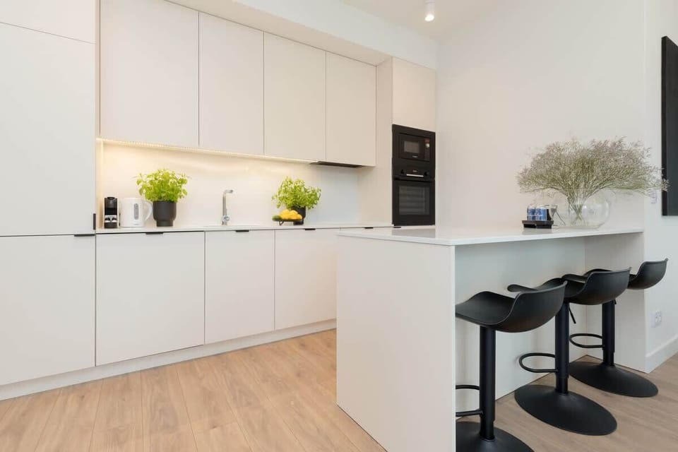 A minimalist white kitchen with clean cabinets and natural wood flooring.