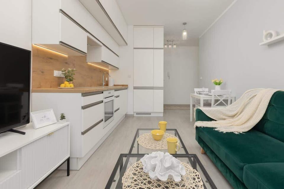 An open-plan living area combining a green sofa, coffee table, and a fully equipped kitchen.

