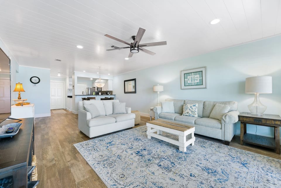 Sink into plush seating in your bright, coastal-inspired living space where gentle ceiling fans and soft lighting create the perfect atmosphere for relaxation.