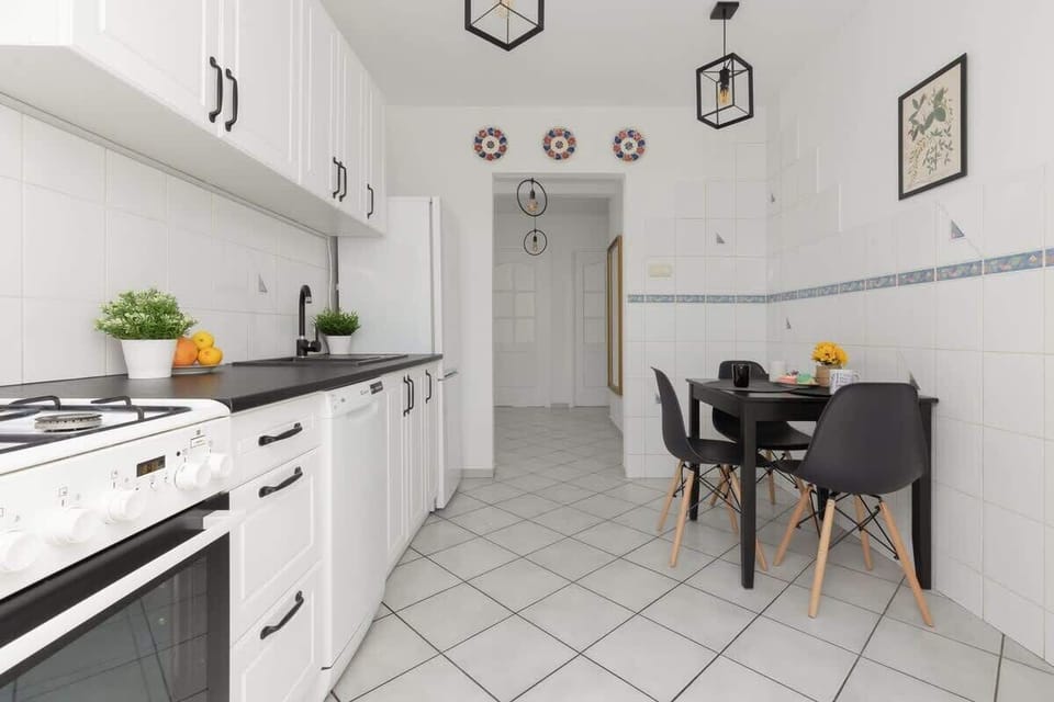 A final view of the kitchen emphasizing its clean white cabinetry, tiled walls, and a welcoming dining area for four.







