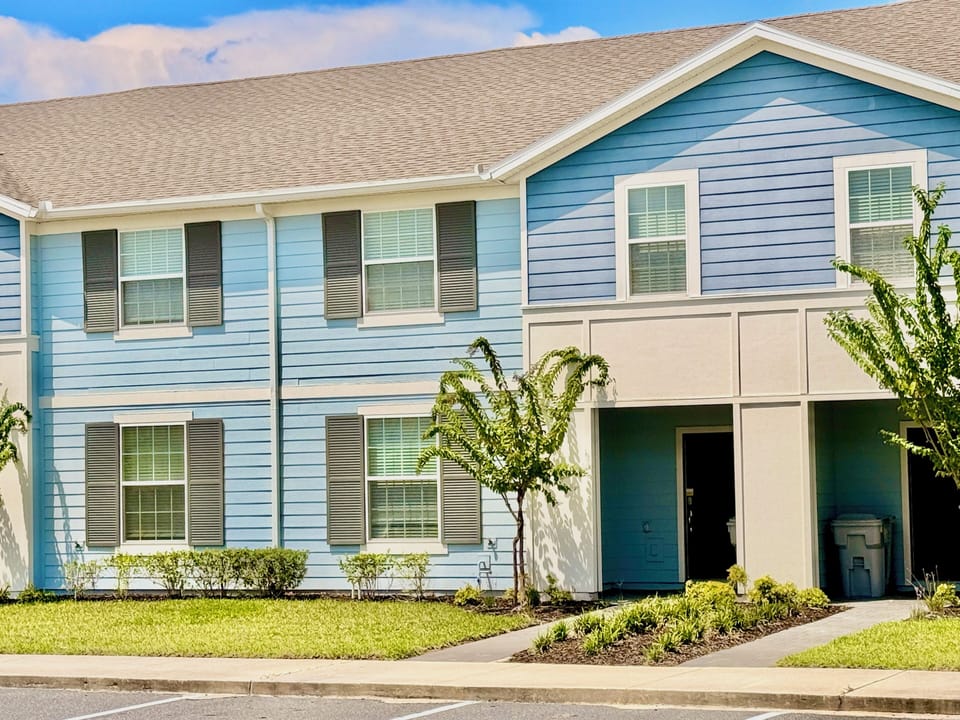 Modern two-story blue home facade with manicured lawn and parking.