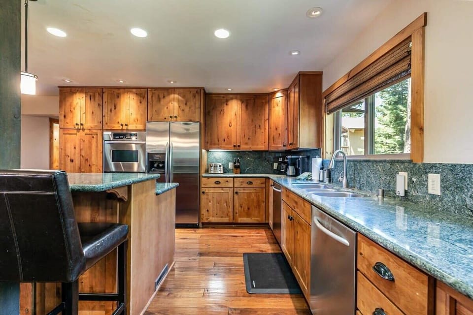 The fully equipped kitchen features stainless steel appliances including two ovens, spacious counters for meal prep, and a kitchen bar with seating for four.