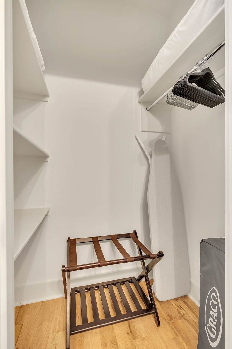 Primary bedroom closet with iron/ironing board, Graco pack-n-play, luggage rack.