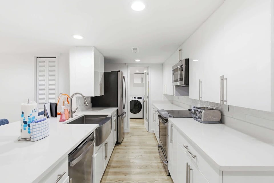 White quartz countertops and sleek minimalist cabinetry create a luminous, airy kitchen for shared meals. Stainless steel appliances and warm wood flooring ground the space, offering a clean and modern heart for your stay.