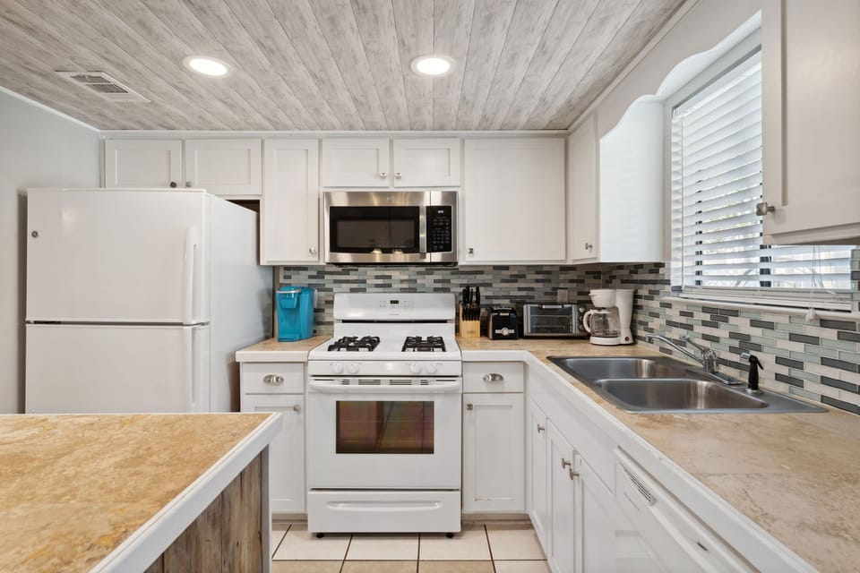 Compact kitchen featuring white cabinetry and modern appliances with a tiled backsplash.