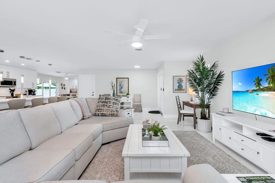 The living area features a 65” flat-screen TV, a large wrap around nap-worthy sofa, a personal desk, chair, and multi-USB outlets and windows that fill the space with natural light.