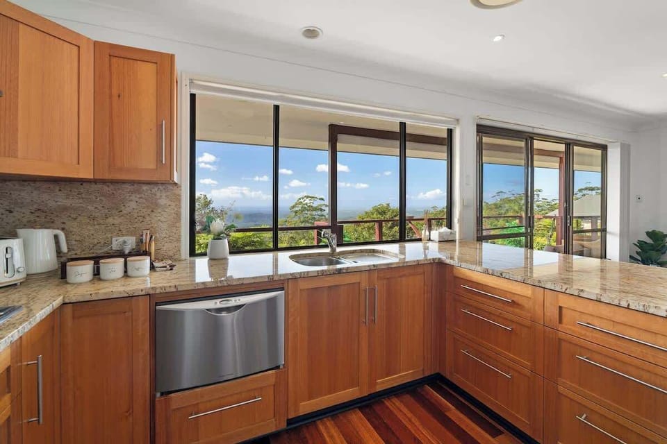 Modern kitchen with stunning views, featuring warm wooden cabinetry. Equipped with a built-in dishwasher, stainless steel sink, and ample storage space, this kitchen is both functional and inviting for cooking and entertaining.