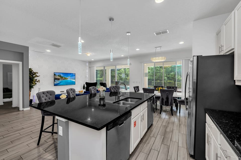 Open layout showcasing the kitchen and living area, including island bar seating and plush velvet dining chairs.
