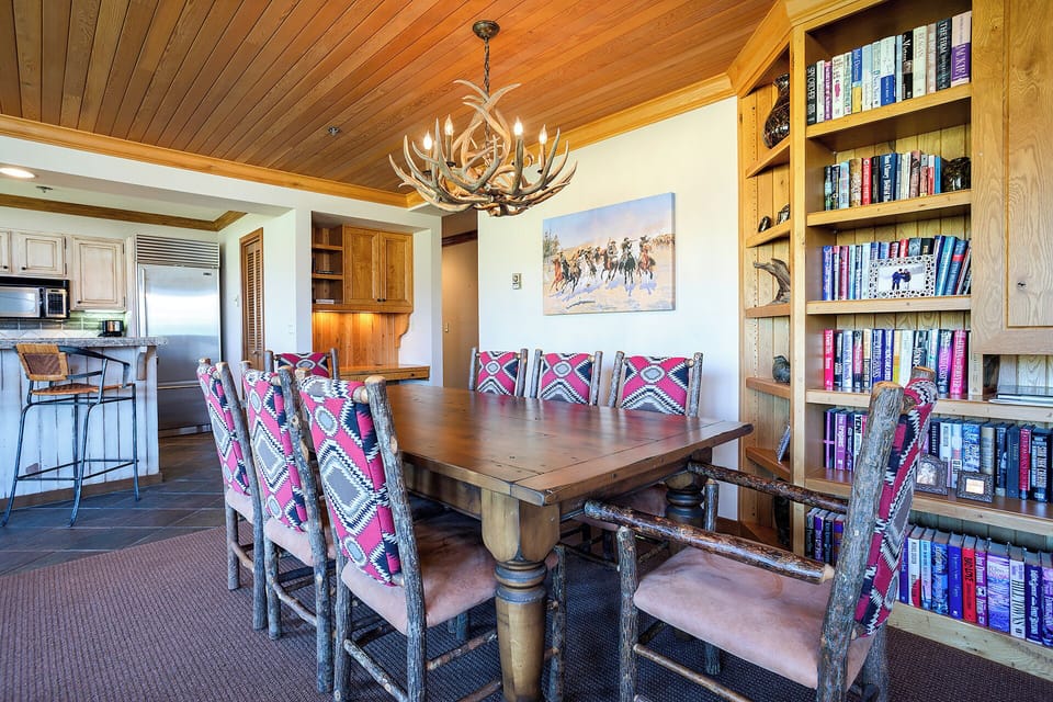 Gather around your rustic dining table beneath an antler chandelier, with floor-to-ceiling bookshelves creating a cozy cabin atmosphere for memorable meals together.