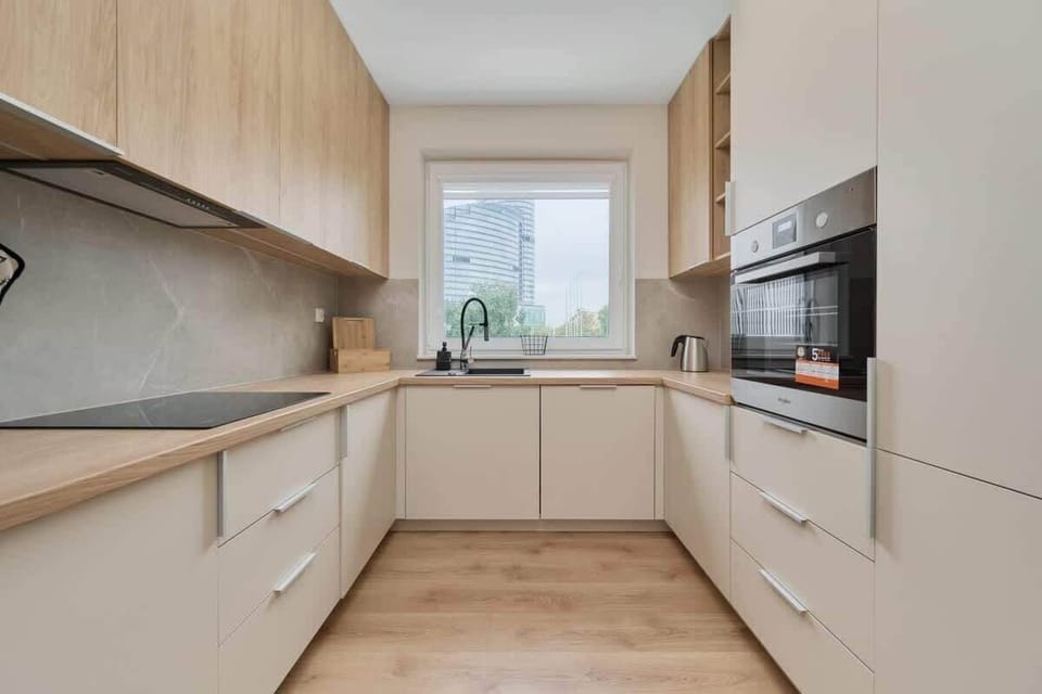 A compact kitchen with light wood cabinets, modern appliances, and a window providing natural light.
